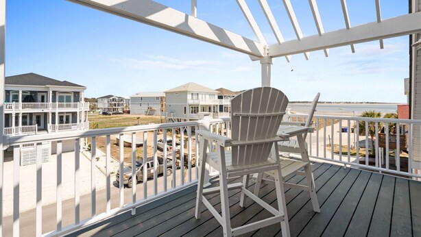Une terrasse en bois avec une chaise blanche, donnant sur un quartier résidentiel avec des maisons et une plage.