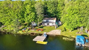 Une maison au bord du lac, avec un quai, un petit bateau et un espace abrité doté de sièges pour l’extérieur.