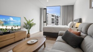 A modern hotel room with a large TV, a sofa, a bed, a balcony with a view of the building, and a potted plant. - Fremantle Coast Studio - Beach at Your Doorstep (Perth)