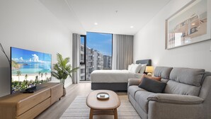 A modern hotel room with a bed, sofa, TV, and a view of a cityscape. - Fremantle Coast Studio - Beach at Your Doorstep (Perth)