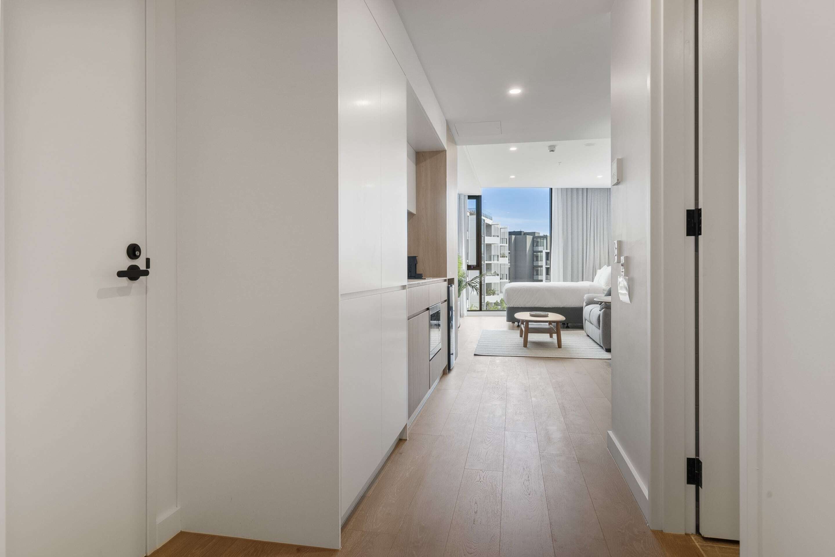A modern, well-lit hallway with a kitchen area, a dining space, and a view of the cityscape through large windows.