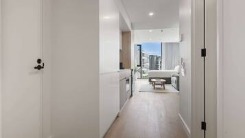 A modern, well-lit hallway with a kitchen area, a dining space, and a view of the cityscape through large windows.