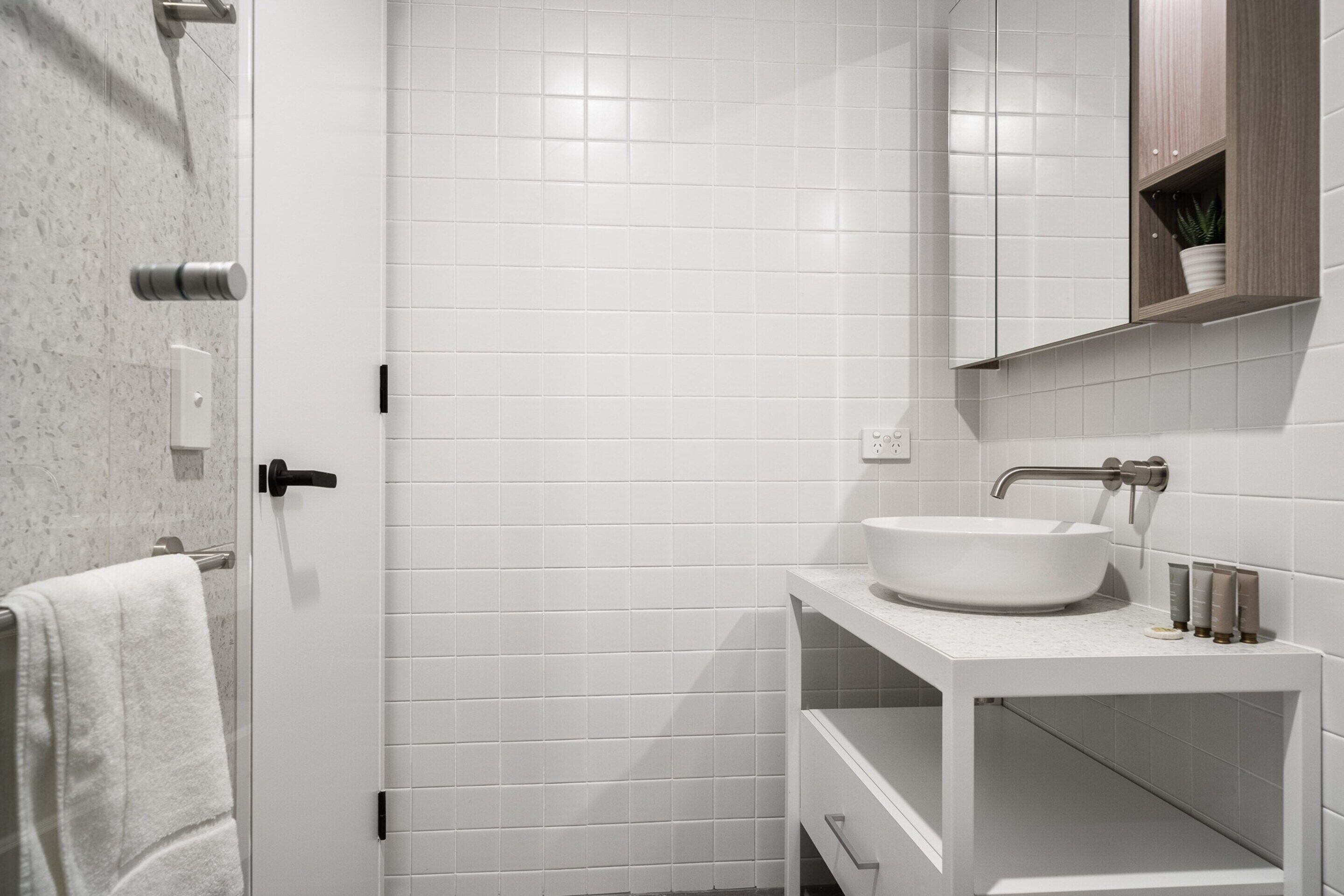 Un baño moderno con azulejos blancos, un lavabo blanco y un armario para espejo.