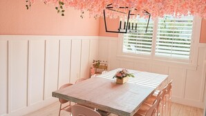 Una zona de menjador amb taula de fusta i cadires roses, envoltada per parets de quadres blancs i un sostre decorat amb flors roses.