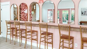 Habitació amb una paret de ratlles roses, un terra de fusta i una zona de bar amb quatre cadires de bambú.