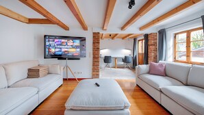 A modern living room with a TV, sofas, and a brick wall. - Stube & Stories - Heritage Riverside Home (Garmisch-Partenkirchen)