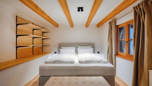 A bedroom with a bed, a bench, wooden shelves, a window, and a ceiling light. - Stube & Stories - Heritage Riverside Home (Garmisch-Partenkirchen)
