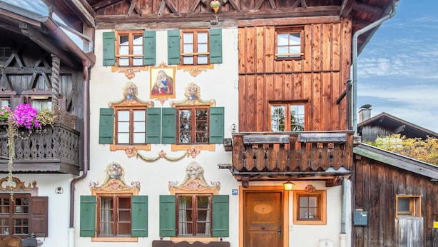 A traditional wooden building with a sloped roof, multiple windows with shutters, and a balcony with a wooden railing. - Stube & Stories - Heritage Riverside Home (Garmisch-Partenkirchen)