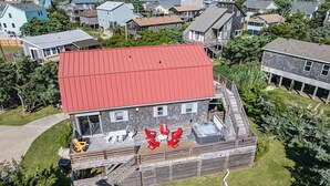 Una casa de dos pisos con techo rojo, una terraza con mobiliario exterior y un jacuzzi.