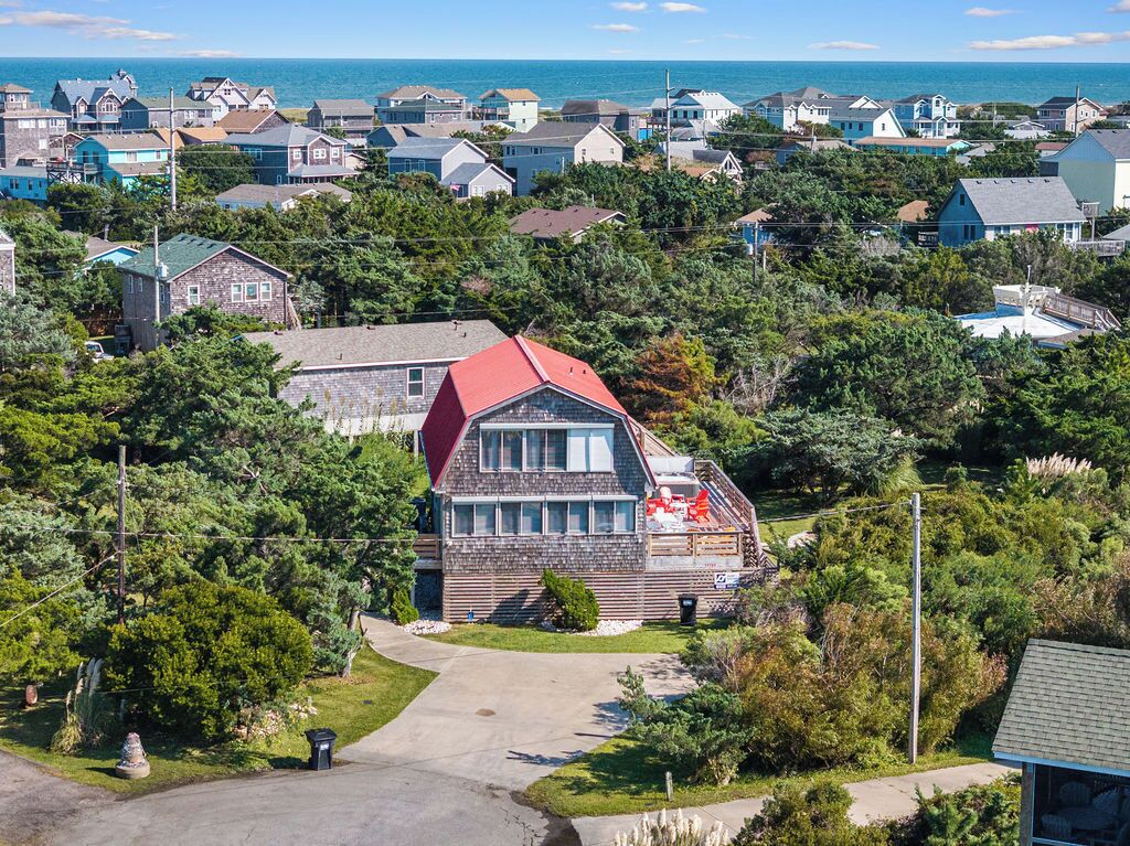 A coastal residential area with a prominent house featuring a red roof, stone walls, and a large window.