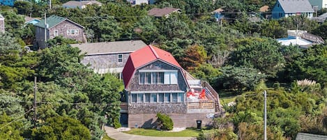 A coastal residential area with a prominent house featuring a red roof, stone walls, and a large window.