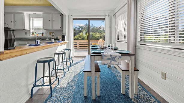 A modern kitchen with a central island, bar stools, and a view through the glass door. - Charming dog-friendly cottage w/ Hot Tub, Smart TVs, Community Pool & Pickleball (Avon)