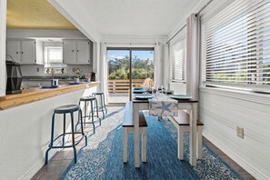 A modern kitchen with a central island, bar stools, and a view through the glass door.