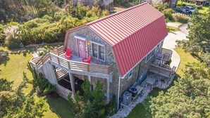 A two-story wooden cabin with a red roof, a deck, and a small porch. - Charming dog-friendly cottage w/ Hot Tub, Smart TVs, Community Pool & Pickleball (Avon)