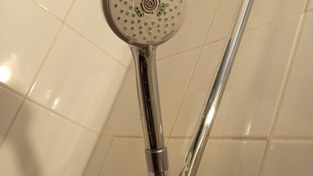Une douche avec un pommeau rond et une poignée en chrome.