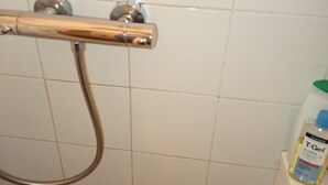 Un baño con azulejos blancos, un cabezal de ducha y una botella de T-Gel en un estante.