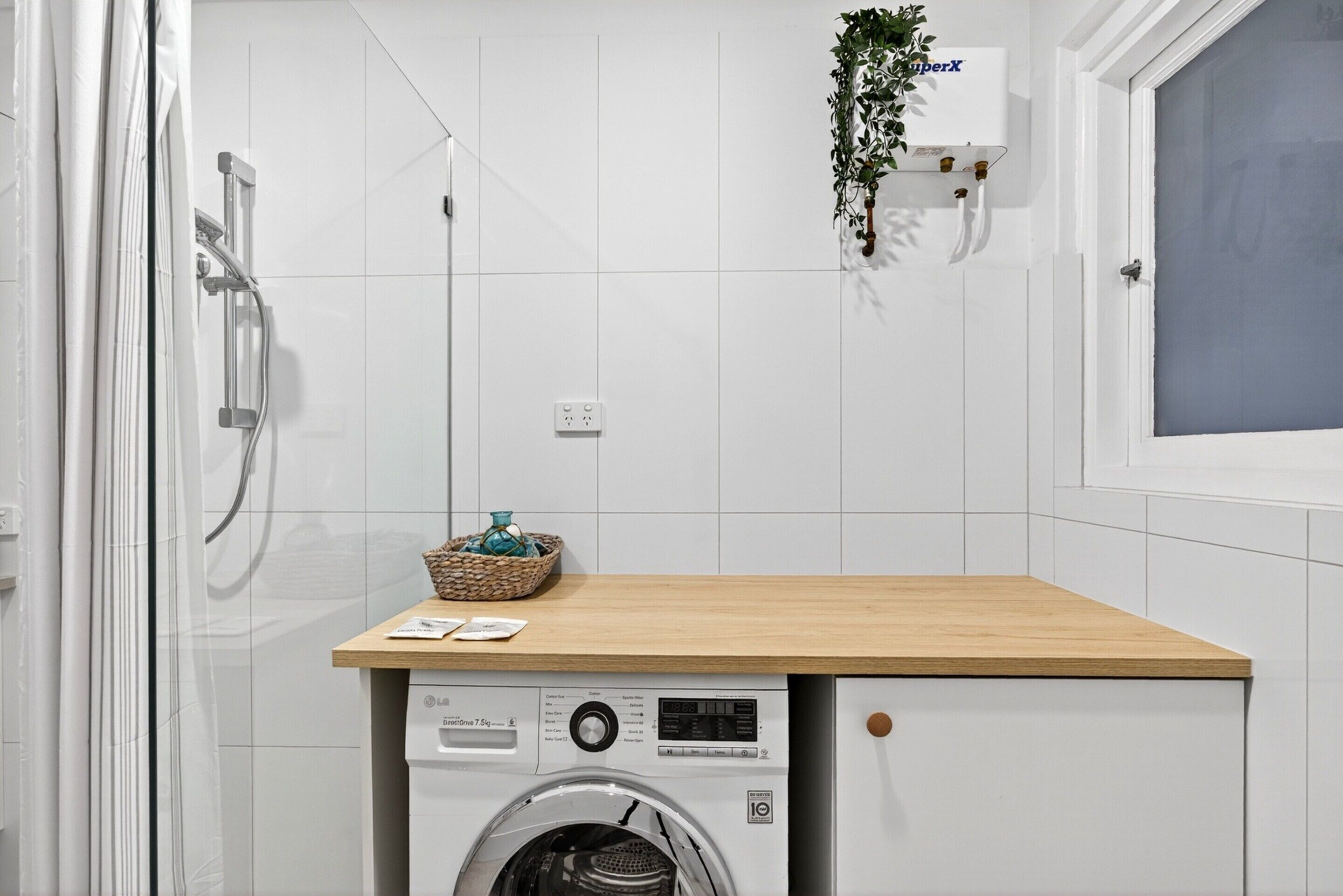 A compact laundry area with a washing machine, a wooden countertop, and a hanging plant.