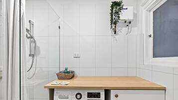 A compact laundry area with a washing machine, a wooden countertop, and a hanging plant.