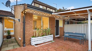 A house with a brick exterior, a covered patio with string lights, a white bench, and a potted plant. - Bright 2-bed Unit Near Scarborough Beach (Perth)