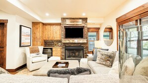 Un salon chaleureux avec une cheminée en pierre, des meubles en bois, un téléviseur à écran plat et des sièges confortables.