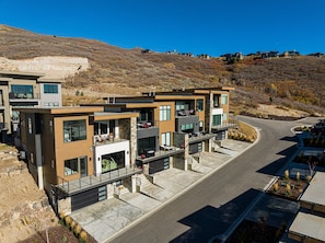 A modern multi-story residential building with balconies, a driveway, and a hilly backdrop.