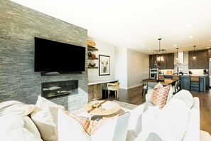 A modern living room with a flat-screen TV, fireplace, sofa, and dining area.