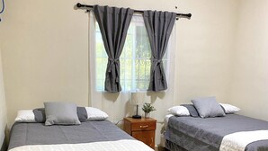 A bedroom with two beds, each with a grey bedspread and white pillows. There is a nightstand with a lamp and a small plant between the beds. - Amazing 3 bedroom house with AC in delightful El Salvador in El Truinfo (El Salvador)