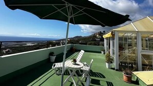 A rooftop terrace with a table and chairs, a green umbrella, and a greenhouse.