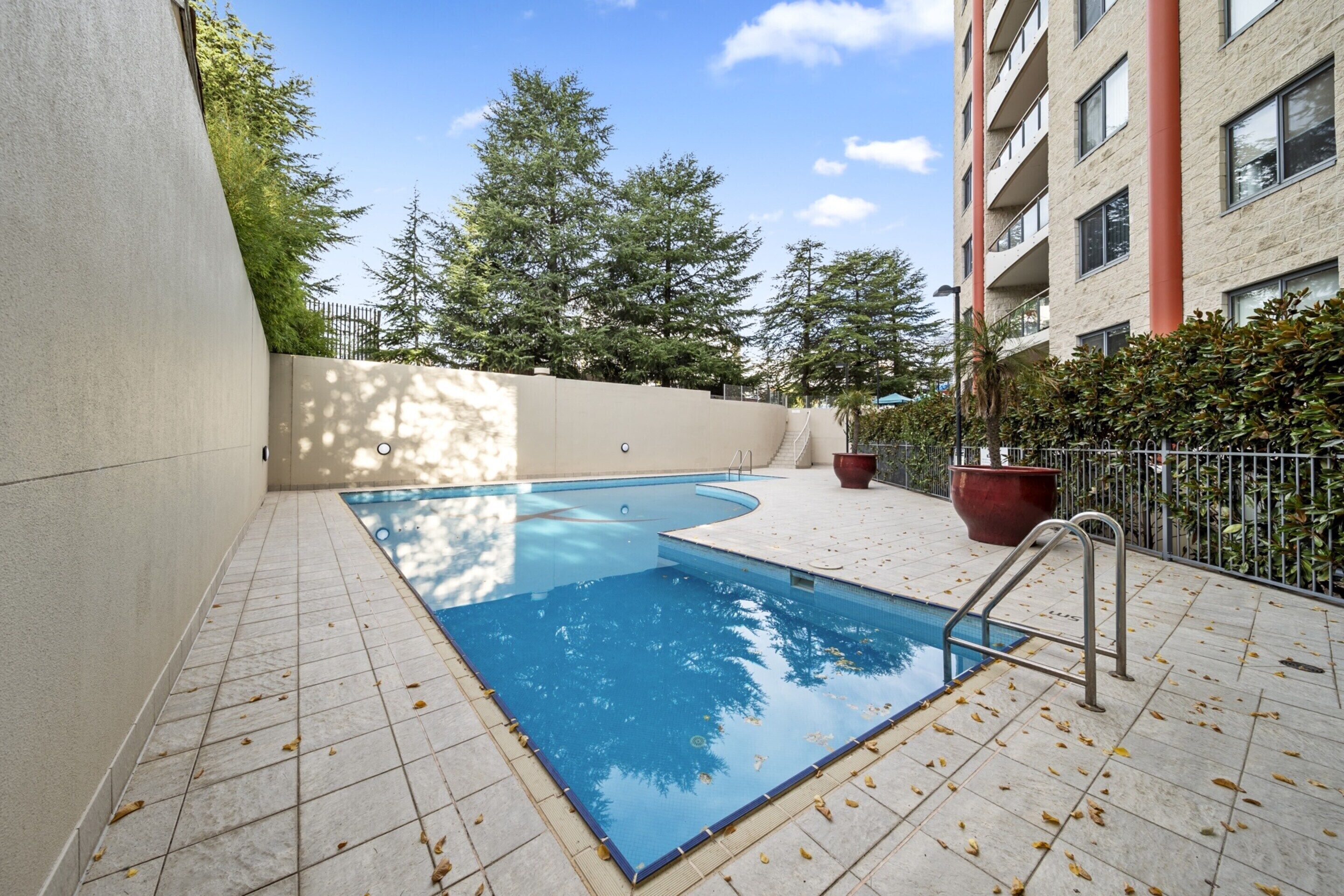 A swimming pool with a tiled deck, surrounded by a low wall and trees.