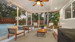 Un'area patio coperta con mobili da esterno, una ventola a soffitto e una piscina sullo sfondo.