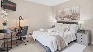 Un dormitorio con cama, escritorio, silla y televisor de pared mostrando 'NETFLIX'.