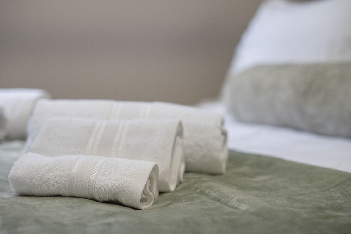 Ein ordentlich bezogenes Bett mit weißen Handtüchern und einer grünen Tagesdecke.