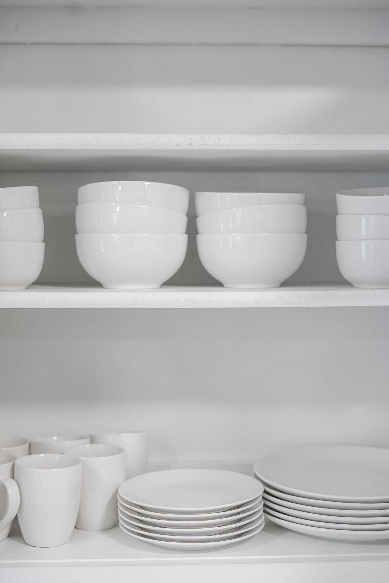 Une étagère blanche sur laquelle sont empilés des bols et des assiettes blancs.