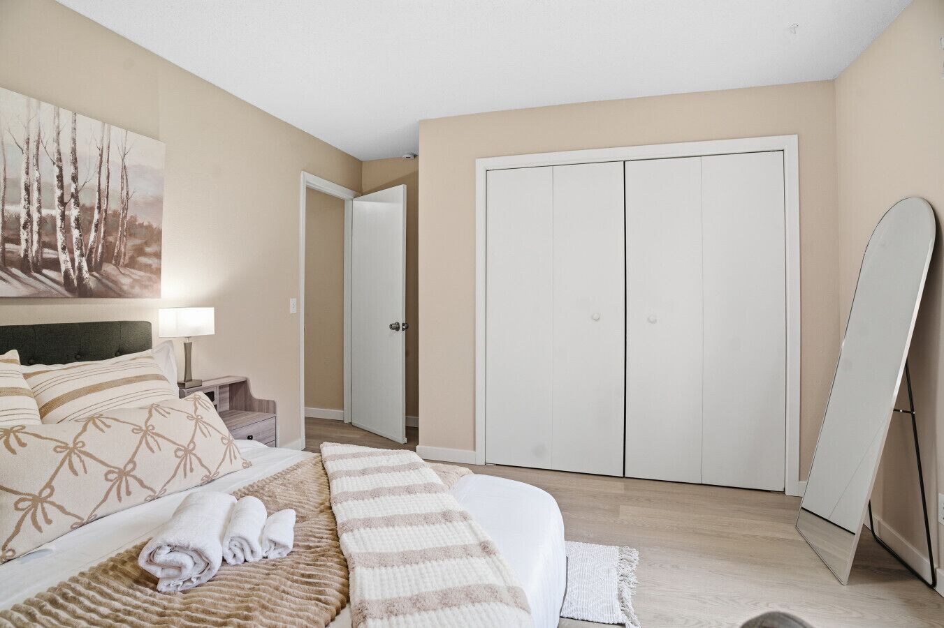 Une chambre à coucher avec un lit, une table de chevet, une lampe, un tableau, une armoire et un miroir.