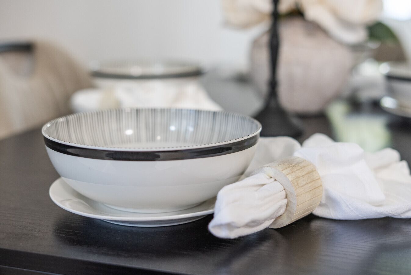 A white bowl with a black rim on a dark surface, accompanied by a white cloth and a wooden object.