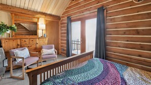 Ein Blockhauszimmer mit einem Bett, zwei Stühlen, einem Schreibtisch und einer Treppe.