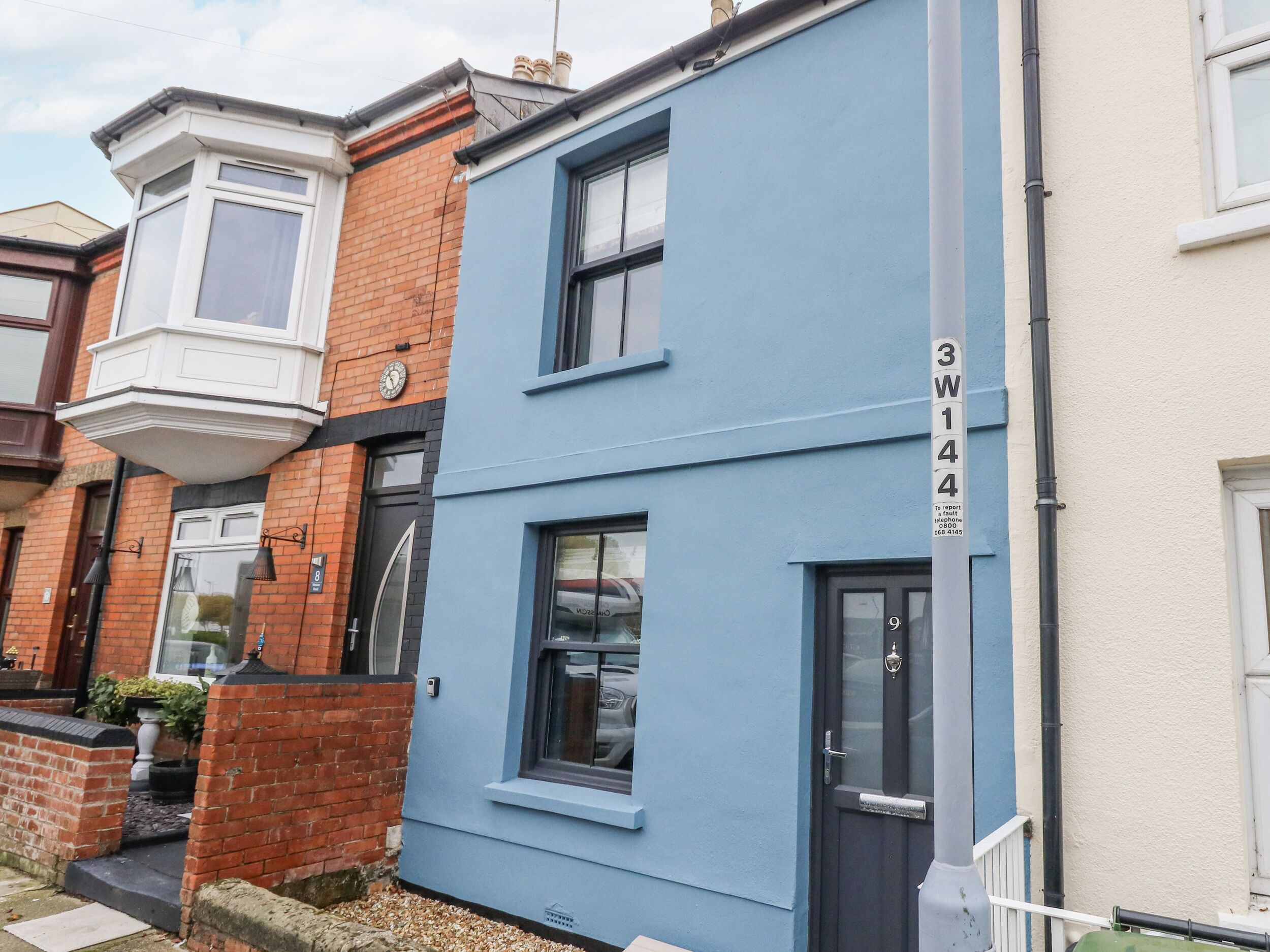 A two-story residential building with a blue facade, a visible number '3W144', and a traditional corner window.