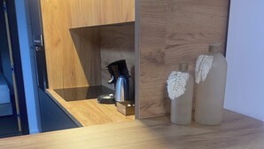 Un área de cocina con armarios de madera, un hervidor de acero inoxidable y dos botellas decorativas en una estantería.