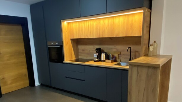 Una cocina moderna con armarios oscuros, encimera de madera y horno empotrado.