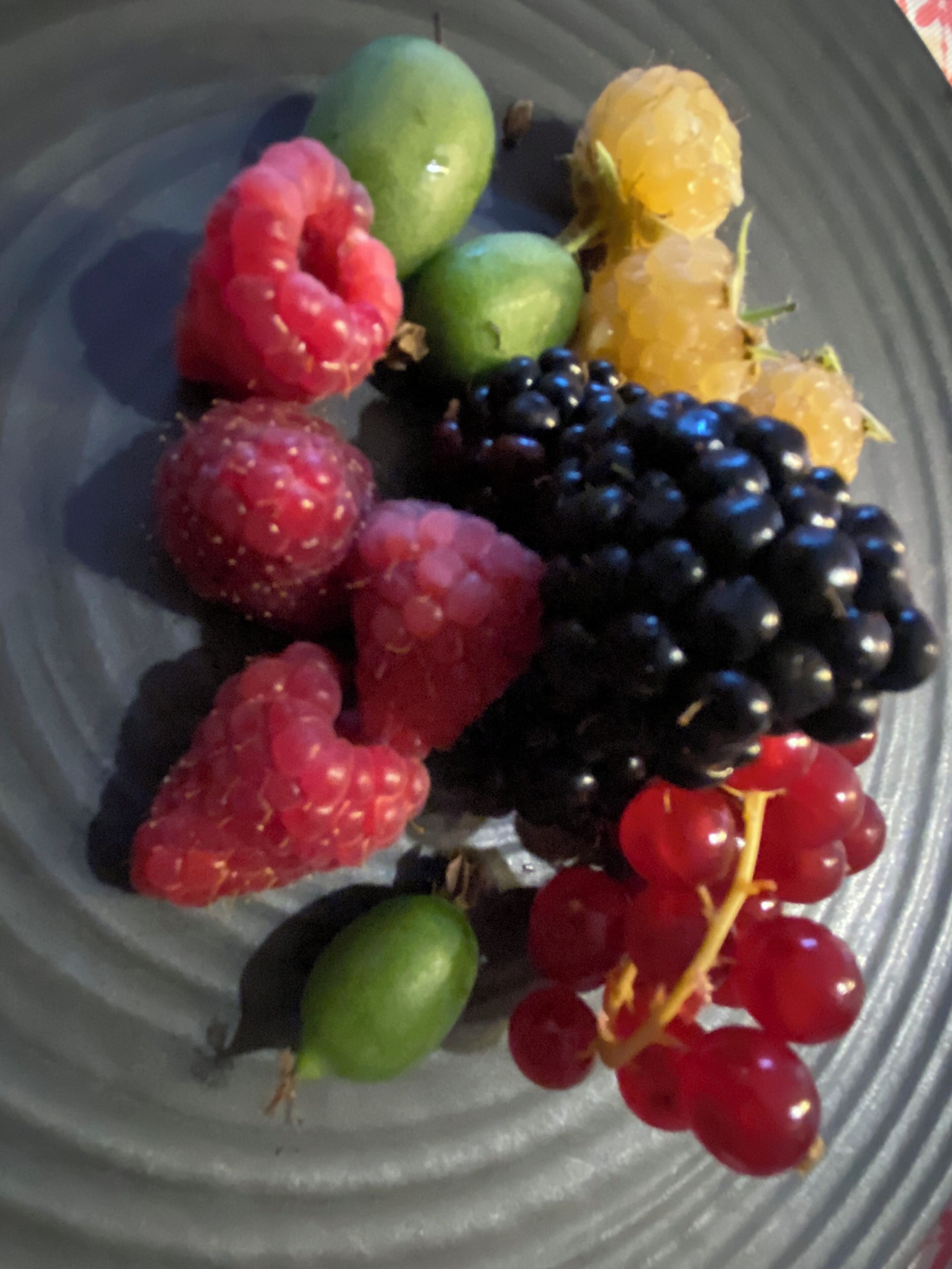 Une assiette contenant divers fruits, notamment des framboises, des mûres, des raisins et un citron.
