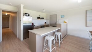 A modern kitchen with a central island, white bar stools, and a refrigerator. - Spacious 3-bed Ground Level Beachside Stay (Middleton)
