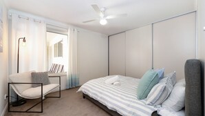 A bedroom with a bed, a chair, a ceiling fan, and a window with curtains. - Spacious 3-bed Ground Level Beachside Stay (Middleton)