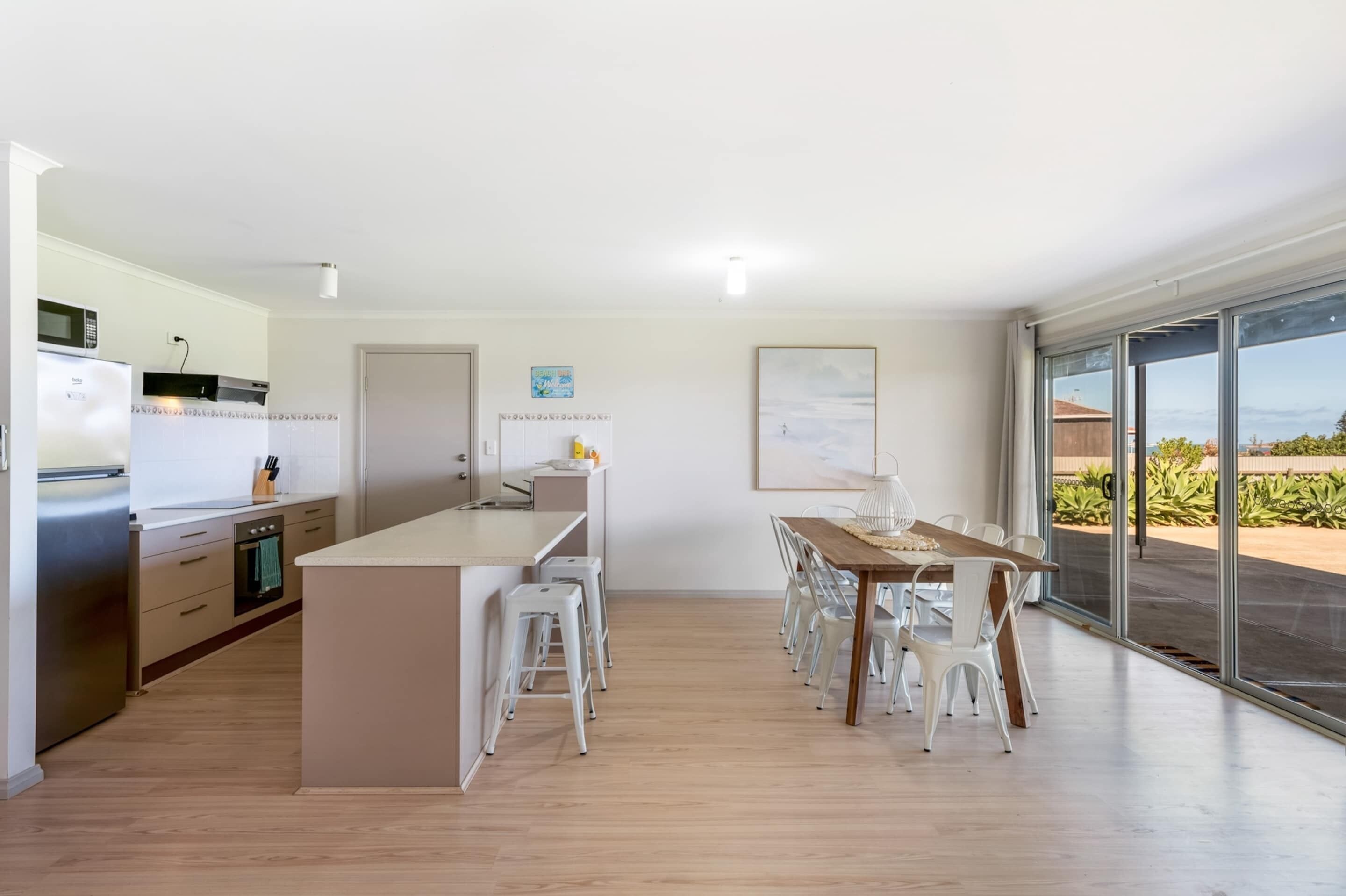 A modern kitchen with a central island, white bar stools, and a dining table with chairs.