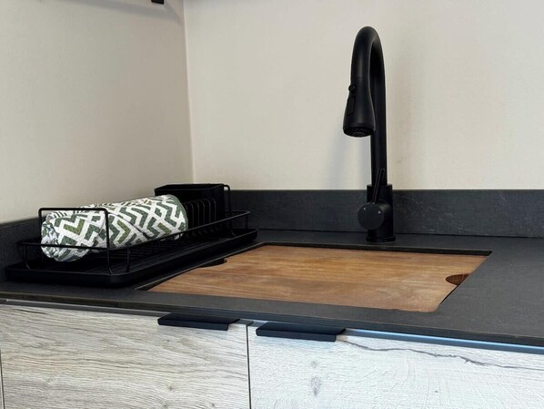 A kitchen with a black faucet, a wooden cutting board, and a black tray with a patterned cloth.