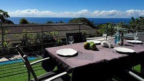 An outdoor dining area with a table set for two, overlooking a pool and a view of the ocean.
