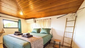 A bedroom with a bed, a window, a ladder, and a small table.