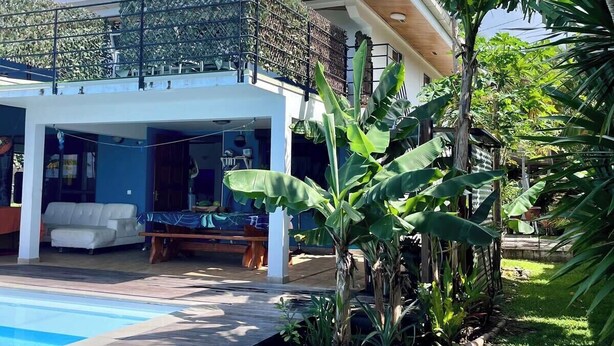 A modern house with a pool, a covered outdoor seating area, and lush greenery.