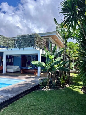 Una casa moderna con piscina, zona de estar exterior cubierta y exuberante vegetación.