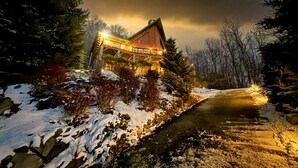 Eine Holzhütte, umgeben von verschneitem Gelände und Bäumen, mit einem Weg dorthin.
