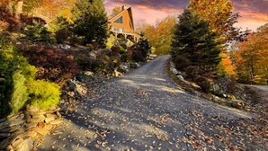 Ein Haus mit geneigtem Dach, umgeben von Herbstlaub und einem steinernen Weg, der dorthin führt.